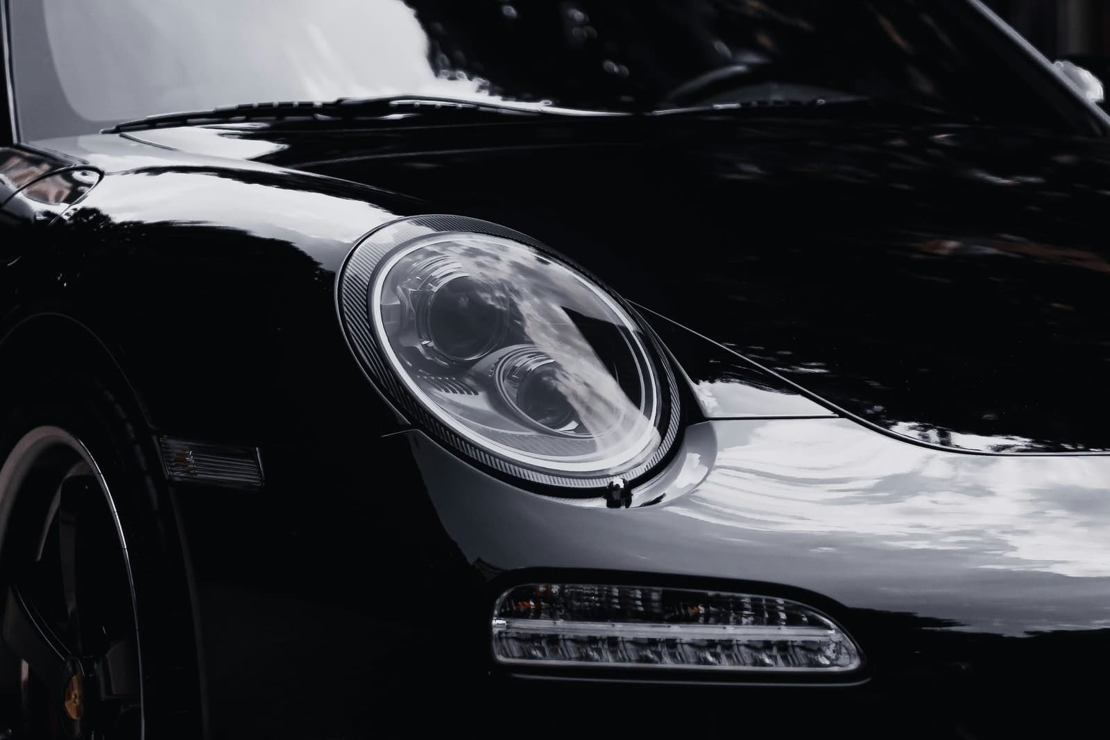 A dark black Porsche 911, front three-quarter, in moody light